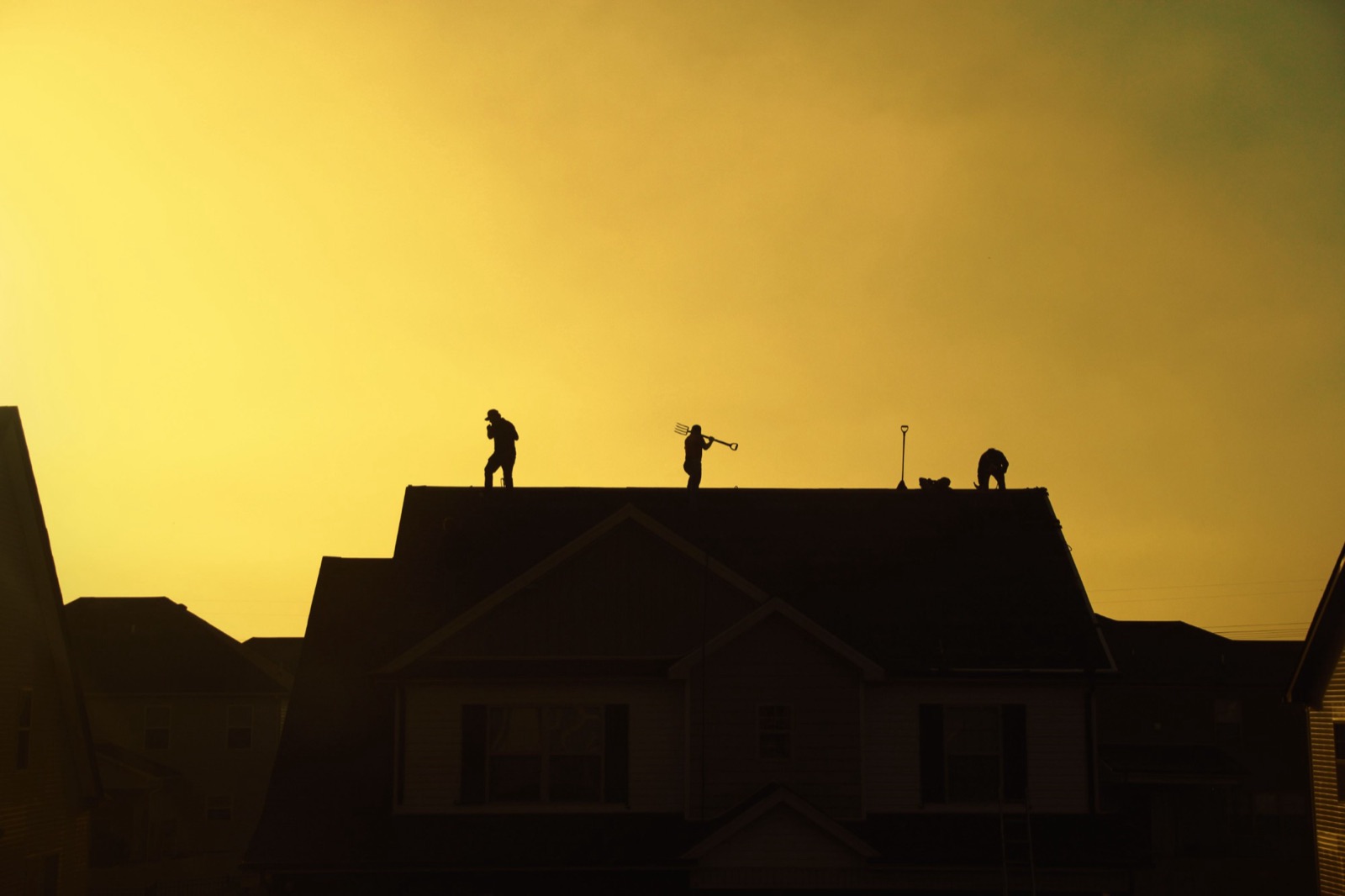 Roofers silhouetted on a rooftop against a golden evening sky